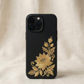 Minimalist luxury iPhone silicone phone case with black matte background featuring a small delicate gold embroidered jasmine flower in the bottom right corner, inspired by traditional South Asian embroidery, fine white thread stitching with realistic raised embroidered texture, elegant minimal composition with lots of negative space