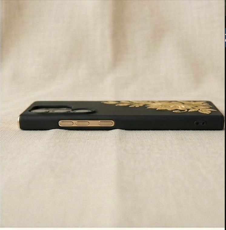 Black phone case with gold floral design on a beige fabric background