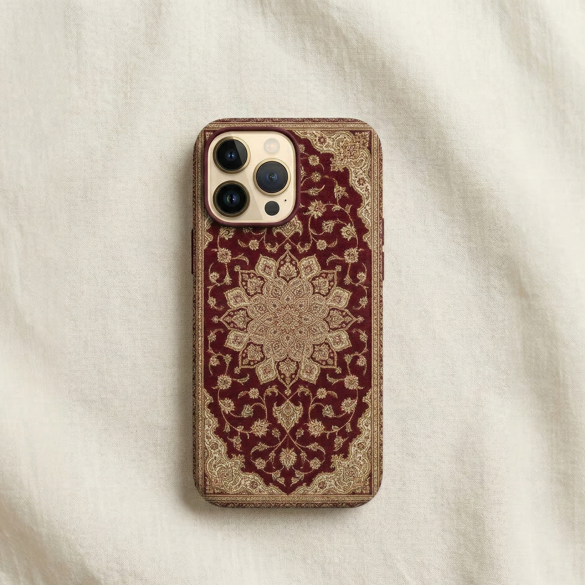 iPhone case inspired by traditional South Asian carpet design, rich deep maroon background featuring an elegant Persian-Mughal style carpet motif with intricate floral medallion in the center and subtle ornamental borders, detailed woven texture inspired by Pakistani and Mughal rugs, refined pattern with gold, ivory, and muted red accents, symmetrical composition, sophisticated cultural aesthetic, photographed as high-end product photography with natural studio lighting on cream backrgound